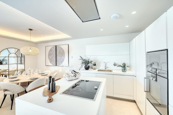 A modern kitchen with a central island, white cabinetry, and a built-in oven.