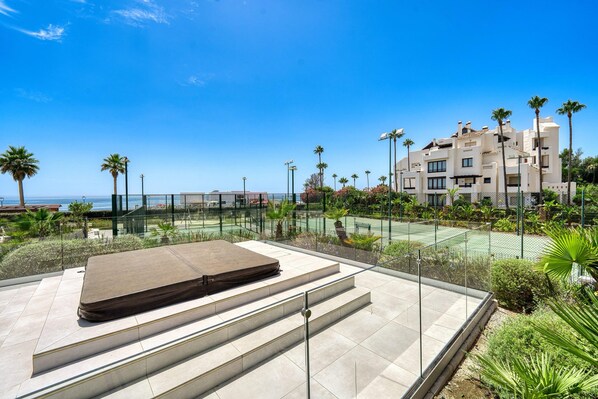 A rooftop terrace with a mattress, steps, and a tennis court in the background.