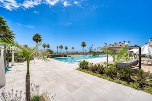A pool area with palm trees, lounge chairs, and a clear blue sky.