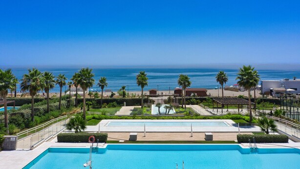 A pool area with a view of the ocean, palm trees, and a building in the background. - 3001 Velaya Beachfront Luxury Apartment (Estepona)