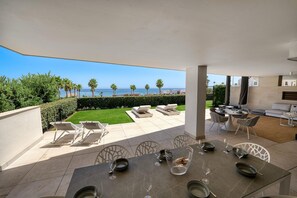 An outdoor patio with a table set for dining, lounge chairs, and a view of the sea.