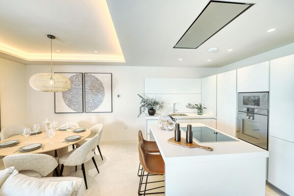 Una cocina moderna con armarios blancos, una isla central y una zona de comedor con una mesa redonda y sillas.