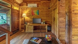 A cozy cabin with wooden walls, a TV, a lamp, and a magazine on the floor. - Alaya Stays Suro Woodbine Chalet Cottage (Kandaghat)