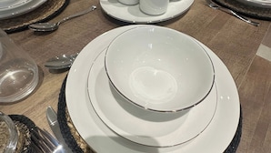 A dining table set with white plates, bowls, and cups, accompanied by cutlery and glassware. - Cosy Birmingham Retreat Near City Centre, Airport (Birmingham)