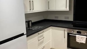 A kitchen with white cabinets, a black countertop, a stainless steel refrigerator, and an oven. - Cosy Birmingham Retreat Near City Centre, Airport (Birmingham)