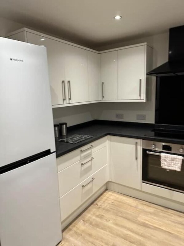 A kitchen with white cabinets, a black countertop, a stainless steel refrigerator, and an oven.