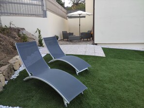 Due poltrone su prato artificiale, con un tavolo e sedie da patio sullo sfondo.