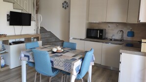 A modern kitchen with a dining area, featuring a flat-screen TV, a microwave, and a sink. - Villa La Dipladenia in Costa Rei (Muravera)