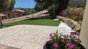 A patio with a stone floor, a flower pot with pink flowers, and a lawn. - Villa La Dipladenia in Costa Rei (Muravera)