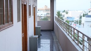 A corridor with a view of buildings in the distance, a railing on the right, and a door on the left. - Hiraa inn Studio Apartments (Kurnool)