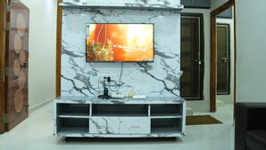 A modern living room with a marble fireplace, a mounted TV, and a built-in entertainment unit. - Hiraa inn Studio Apartments (Kurnool)