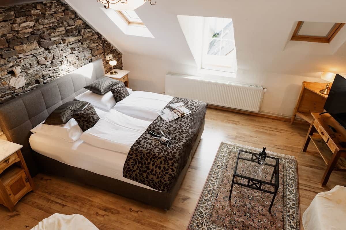 Ein Schlafzimmer mit Steinwand, einem Bett mit Leopardenmuster-Bettwäsche, Holzboden, einem Oberlicht und einem kleinen Tisch mit Lampe.