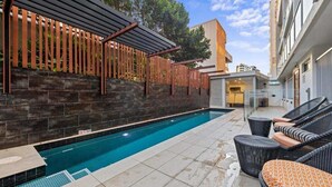 Una piscina con un pérgola, mobiliario exterior y un muro de piedra.