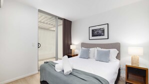 Habitación de hotel con cama, mesita de noche, lámpara, un cuadro en la pared y una puerta corredera.