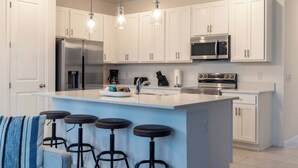 A modern kitchen with white cabinets, stainless steel appliances, a central island with stools, and pendant lighting.