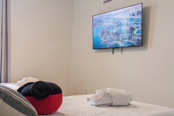 Habitaci ón de hotel con cama, almohadas, televisor montado en la pared y una toalla doblada con cuidado sobre la cama.