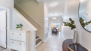 A hallway with a staircase, a dining area in the background, and a mirror on the wall. - Kissimmee 4BR Retreat | Resort Access & Pool (Kissimmee)