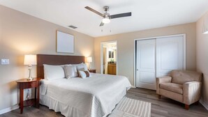 A bedroom with a bed, bedside tables, a ceiling fan, a chair, and a door. - Kissimmee 4BR Retreat | Resort Access & Pool (Kissimmee)