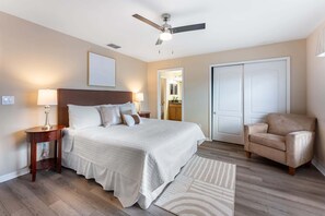 Een slaapkamer met een bed, nachtkastjes, een plafondventilator, een stoel en een deur.