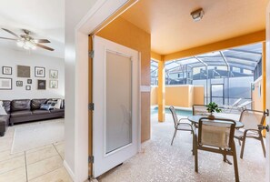 Un salon comprenant un canapé, un ventilateur de plafond et une porte donnant sur un balcon avec une piscine et un espace salon extérieur.