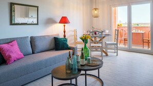 Una sala de estar moderna con un sofá gris, una mesita redonda con botellas, una lámpara roja y una zona de comedor con mesa y sillas.