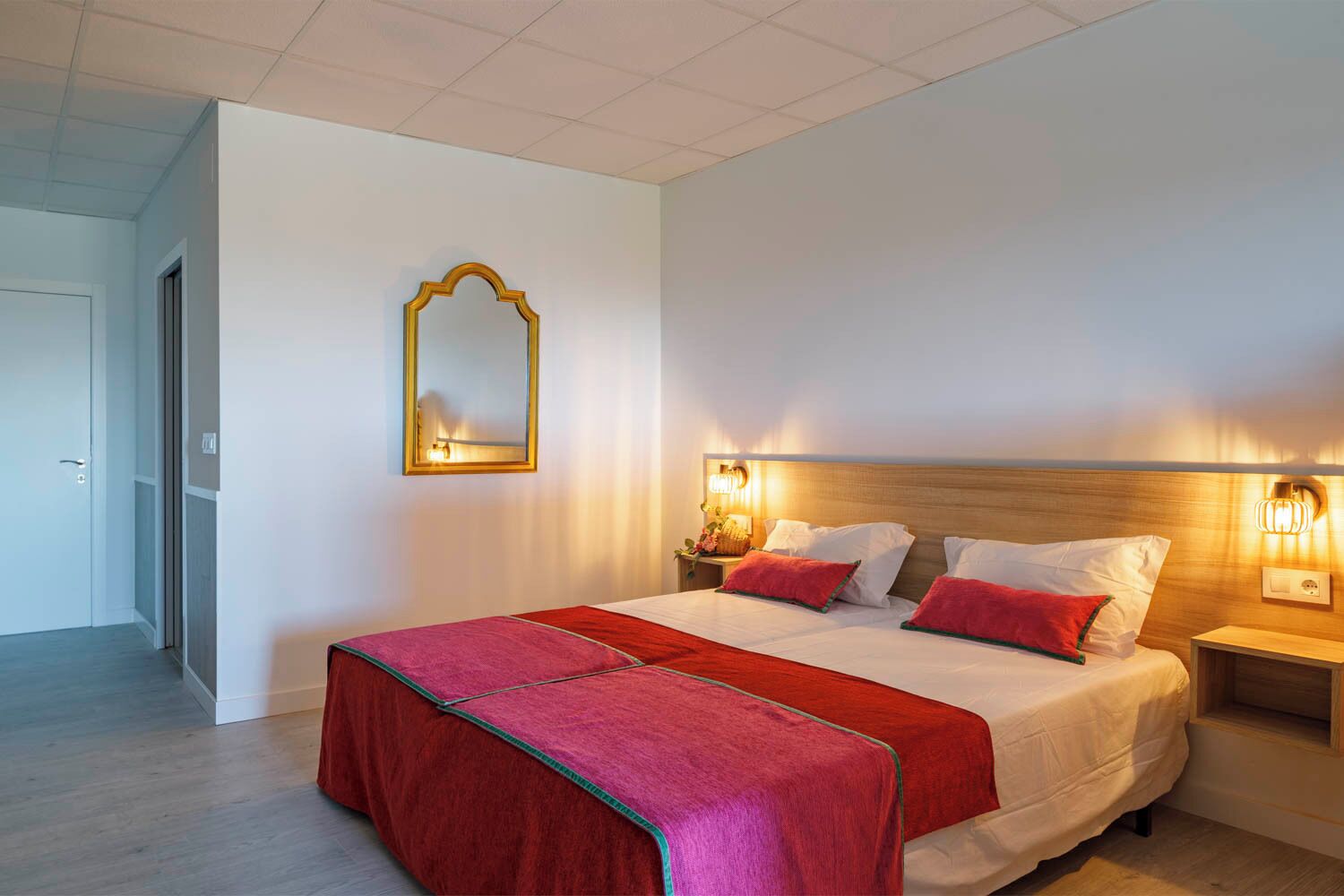 Ein Hotelzimmer mit einem großen Bett, einem Spiegel, Nachttischlampen und einer roten Tagesdecke.