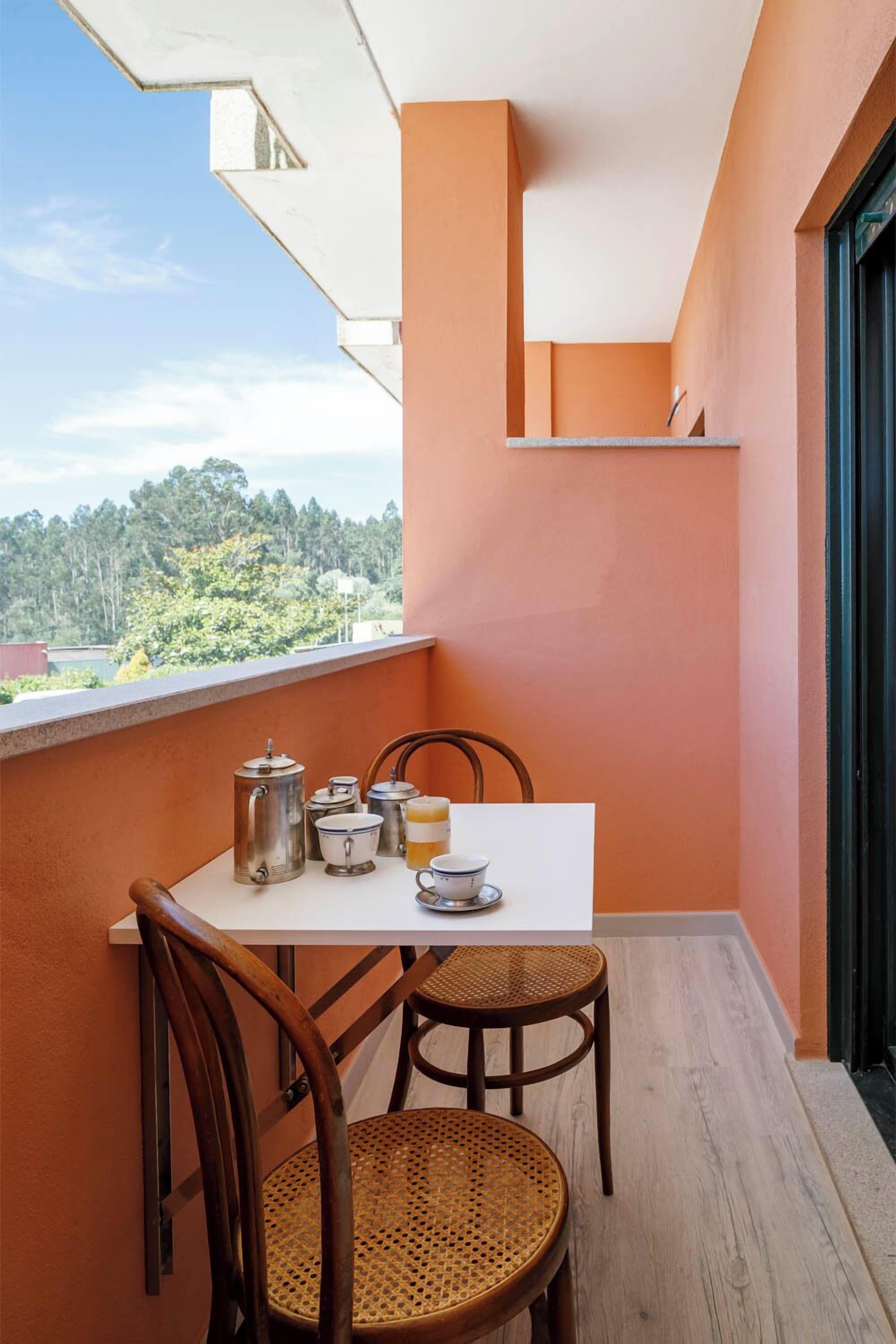 Un balcon avec une table préparée pour le thé, deux fauteuils en osier et une vue sur la verdure.