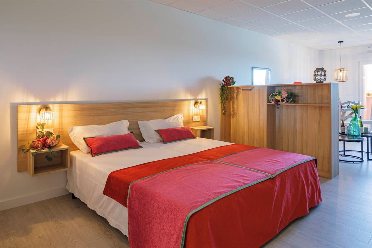 A modern hotel room with a large bed, wooden headboard, bedside tables with lamps, and a small desk with a chair.