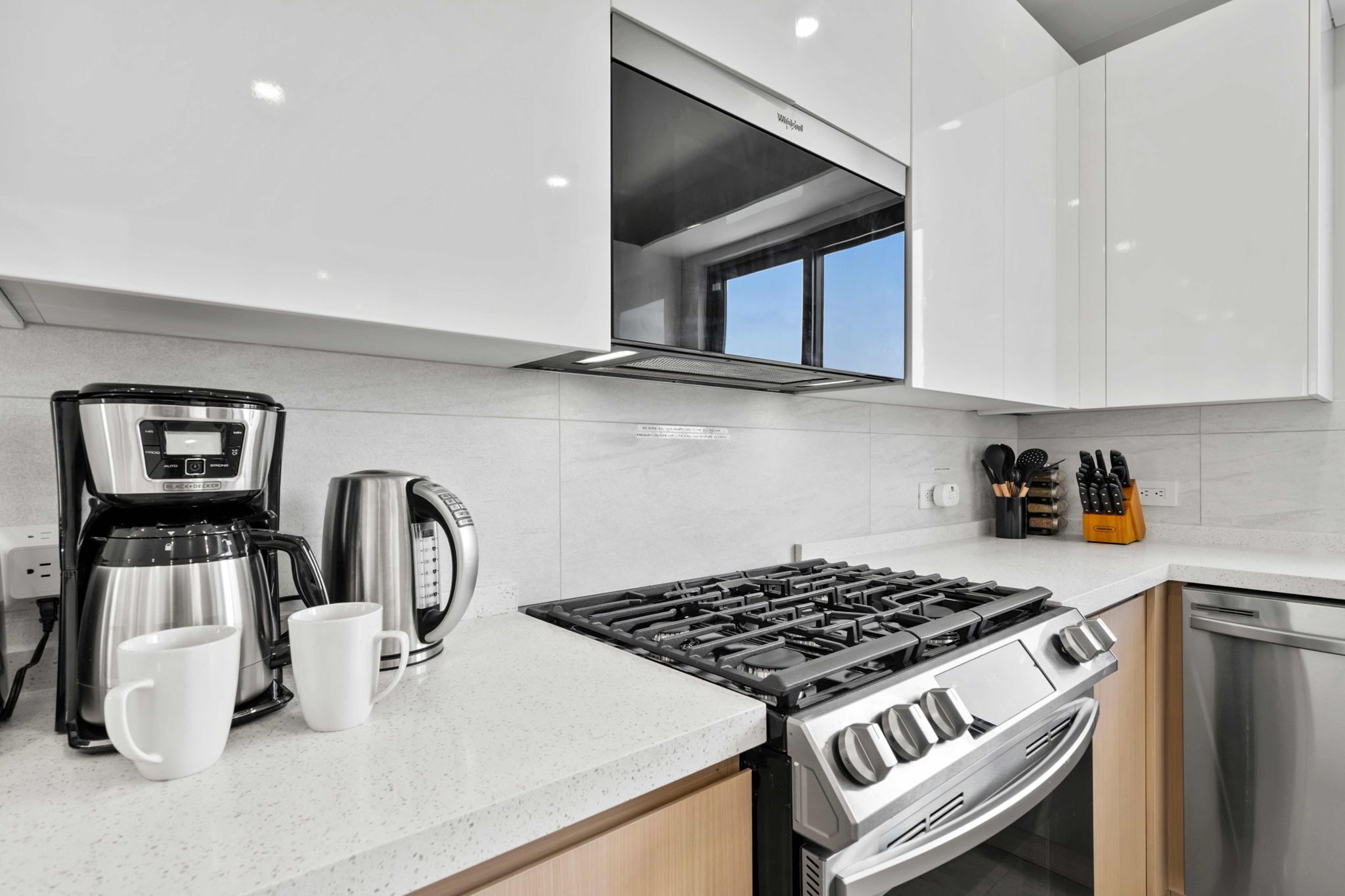 A modern kitchen with white cabinets, a stainless steel stove, a coffee maker, and a toaster.