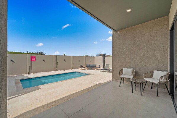An outdoor pool area with a clear blue sky, a pool, and seating arrangements. - Safir 40 (Noord)