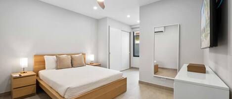 A modern bedroom with a wooden bed, bedside tables with lamps, a ceiling fan, a large mirror, and a TV mounted on the wall.