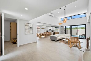 A spacious living area with a large white sofa, a dining table with chairs, and a pool visible through large windows. - Safir 40 (Noord)