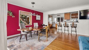 A modern living room with a red accent wall, wooden dining table, and bar stools. - Boho-Style Point Loma Retreat, Large Outdoor Deck (San Diego)