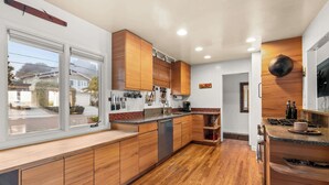 A modern kitchen with wooden cabinets, a built-in dishwasher, and a large window. - Boho-Style Point Loma Retreat, Large Outdoor Deck (San Diego)