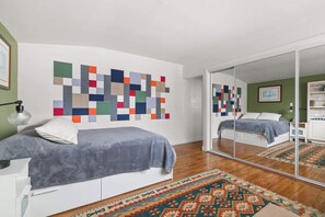 A bedroom with a bed, a mirror, a colorful wall art piece, and a patterned rug. - Boho-Style Point Loma Retreat, Large Outdoor Deck (San Diego)