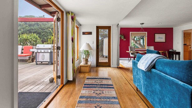An open-plan living area with a wooden deck, a blue sofa, and a view of the outdoors. - Boho-Style Point Loma Retreat, Large Outdoor Deck (San Diego)
