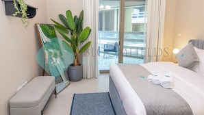 A hotel room with a bed, a bench, a potted plant, a mirror, and a view of the balcony. - Bloomfields Modern 1BR Soul Beach Access (Abu Dhabi)