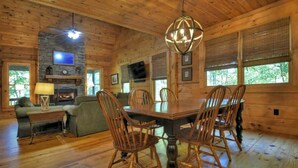 A wooden cabin interior with a dining table, chairs, a fireplace, and a television. - Smokey's Place | $179 Off Your Stay! (Blue Ridge)