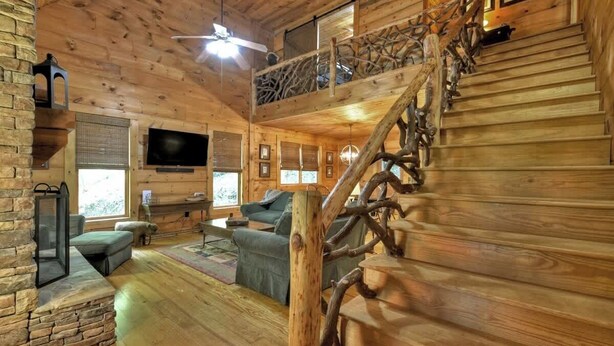 A log cabin interior with a wooden staircase, a ceiling fan, a flat-screen TV, and a cozy seating area. - Smokey's Place | $179 Off Your Stay! (Blue Ridge)