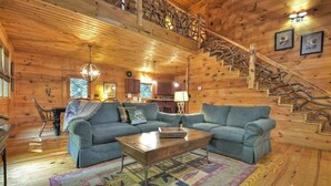 A wooden cabin interior with a staircase, two sofas, a coffee table, and a chandelier. - Smokey's Place | $179 Off Your Stay! (Blue Ridge)