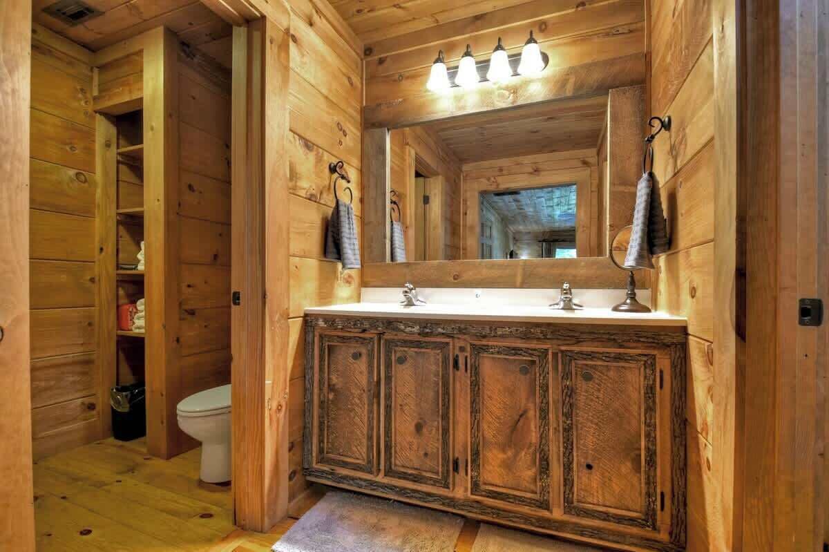 Un baño de cabaña de madera con un lavamanos blanco, tres armarios, un espejo y una toalla colgada en un gancho.