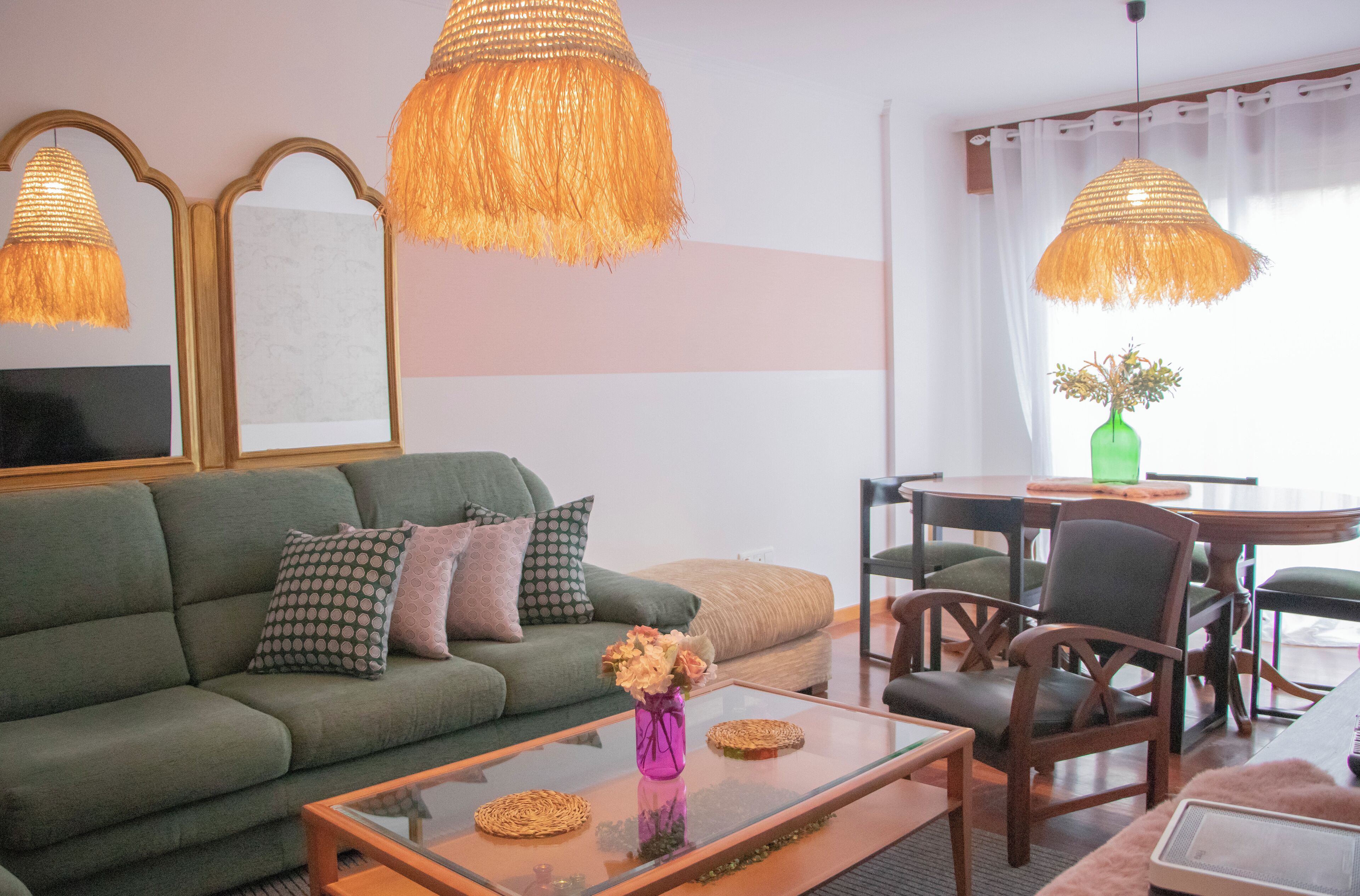Una sala de estar con un sofá verde, una mesa de centro de vidrio con individuales tejidos, y dos lámparas de mimbre.