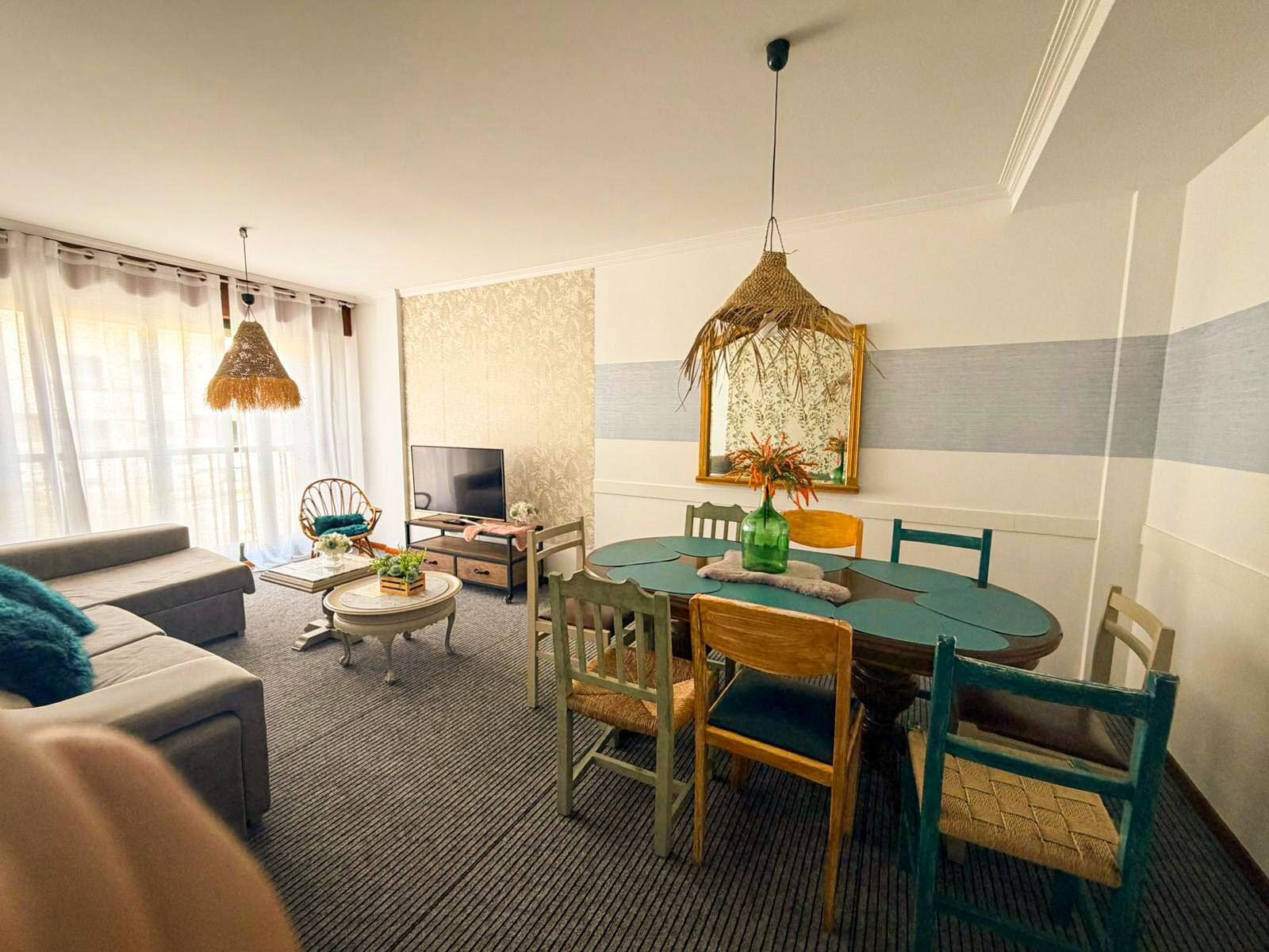 A living room with a sofa, a television, a dining table with chairs, and a hanging light fixture.