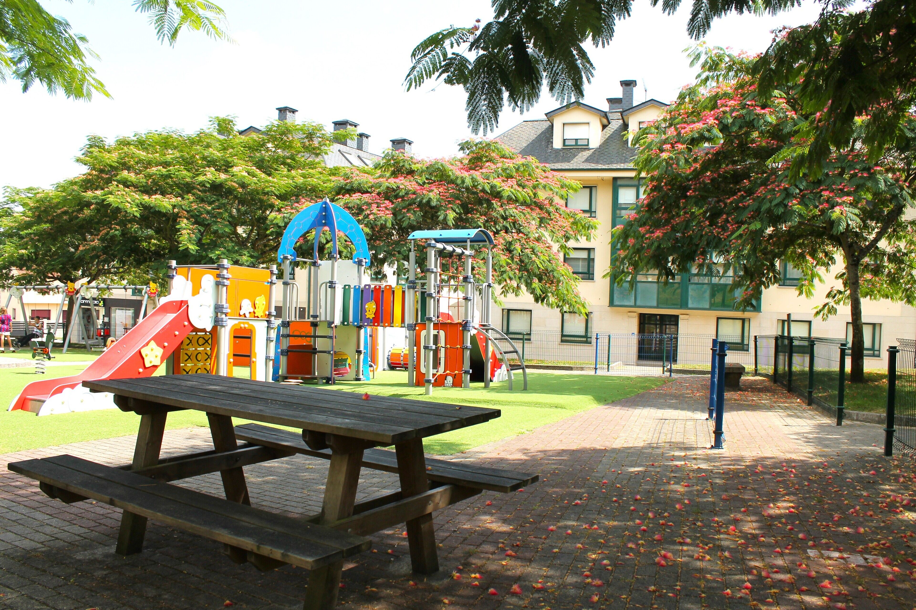 Ein Spielplatz mit verschiedenen Spielgeräten, einem Picknicktisch und einem Gebäude im Hintergrund.