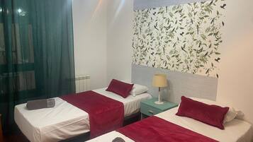 A hotel room with two beds, a window with curtains, a radiator, and a wall with a floral wallpaper.