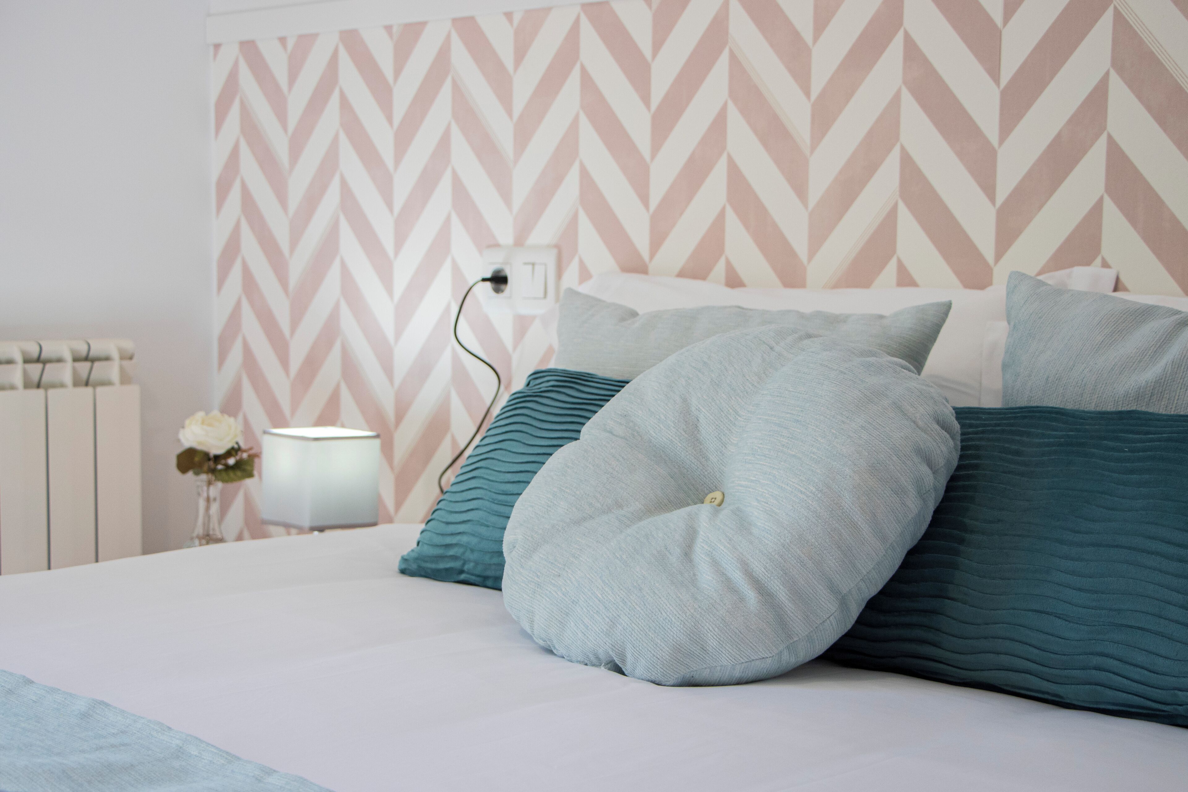 Una cama bien hecha con almohadas y una mesita de noche con lámpara y jarrón.