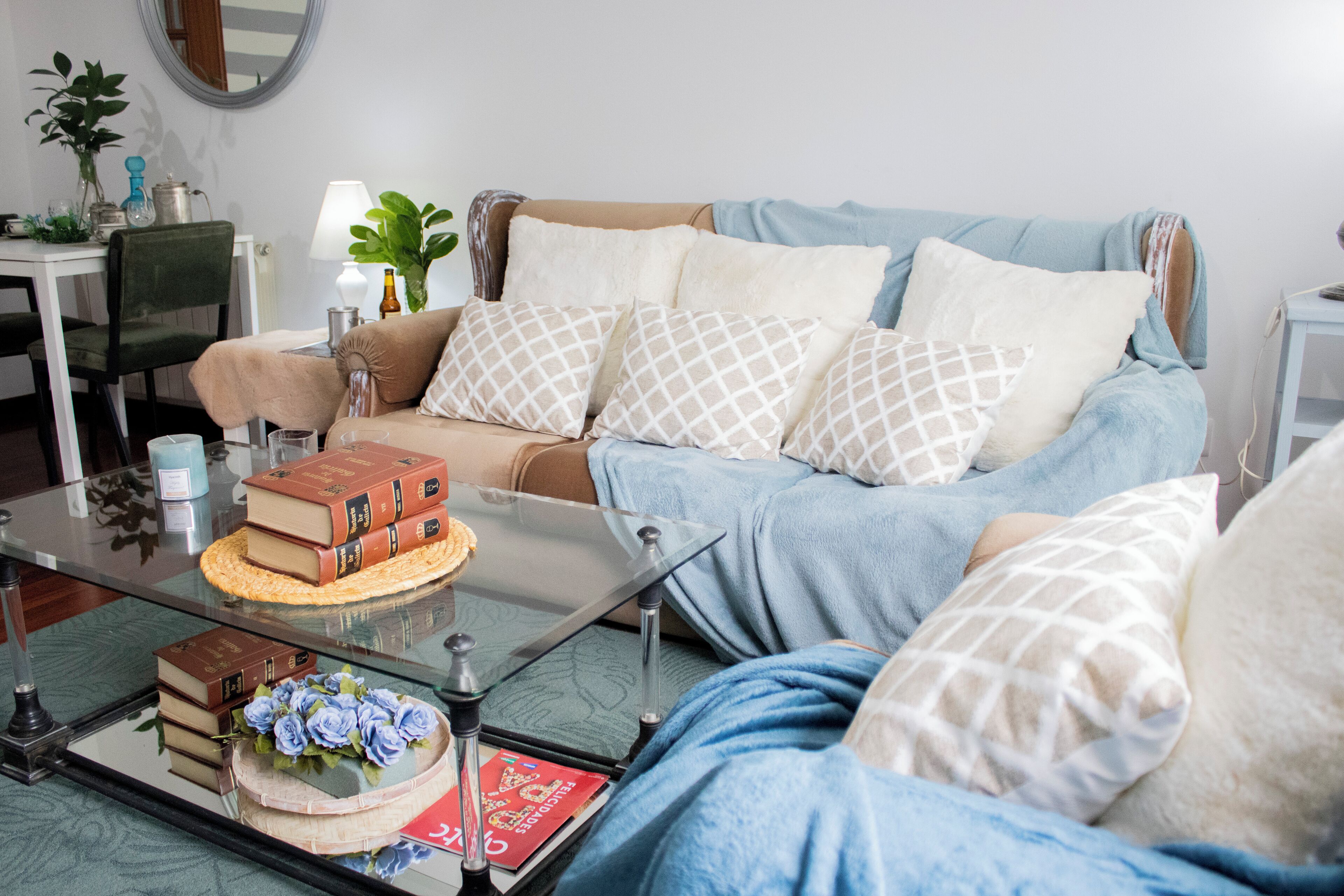A cozy living room with a sofa, a glass coffee table, and a side table with books and a lamp.
