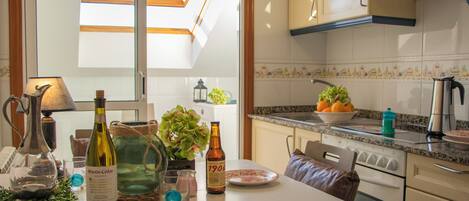 A kitchen with a white countertop, a wine bottle, a glass, a bowl of fruit, and a stove.