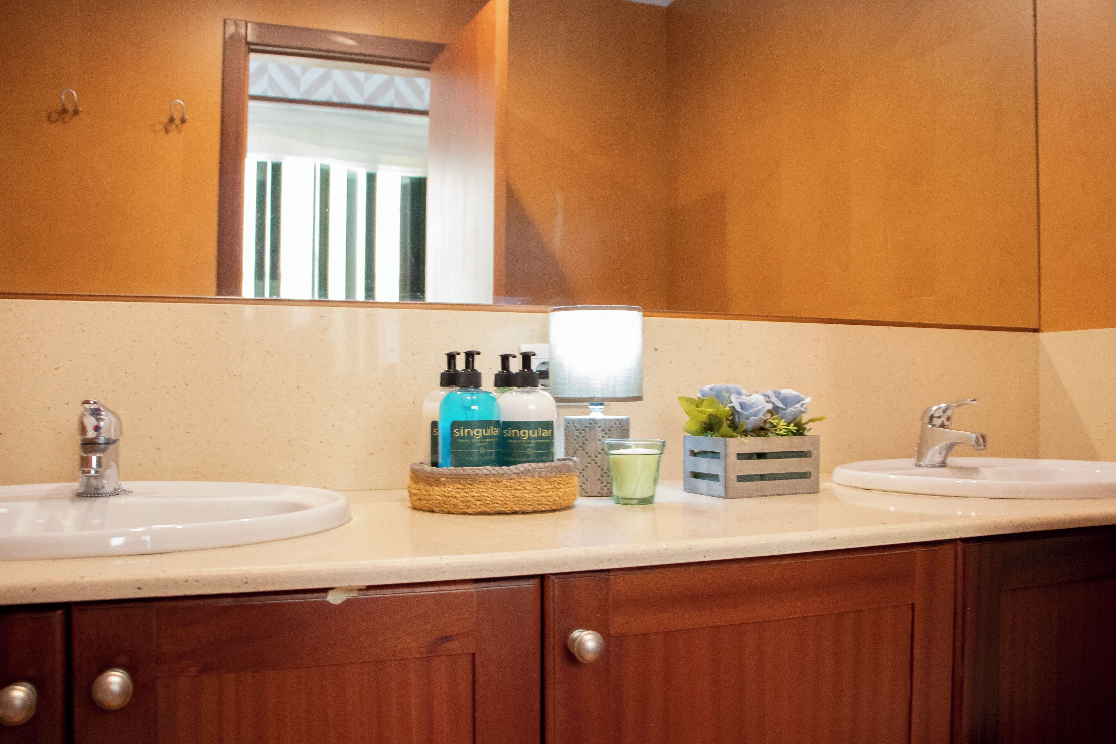 Ein Badezimmer mit zwei Waschbecken, Holzschränken, einem Spiegel und Toilettenartikeln auf der Ablagefläche.