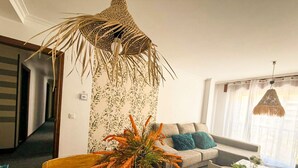 Un salon comprenant un canapé, une table à manger avec des chaises, un luminaire suspendu et un mur orné d’un motif végétal.